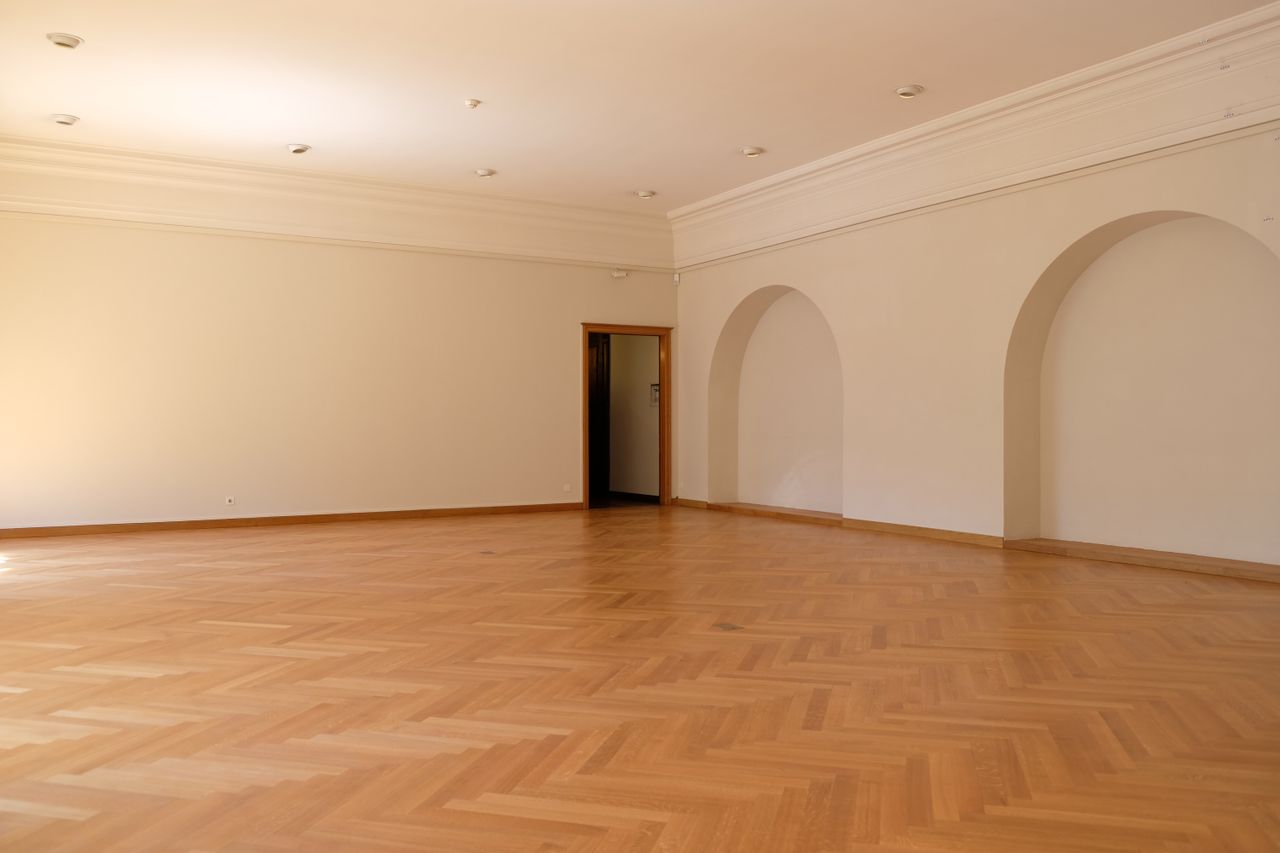 A large empty room with elegant wooden flooring, arches, and natural lighting, perfect for interior design inspiration.